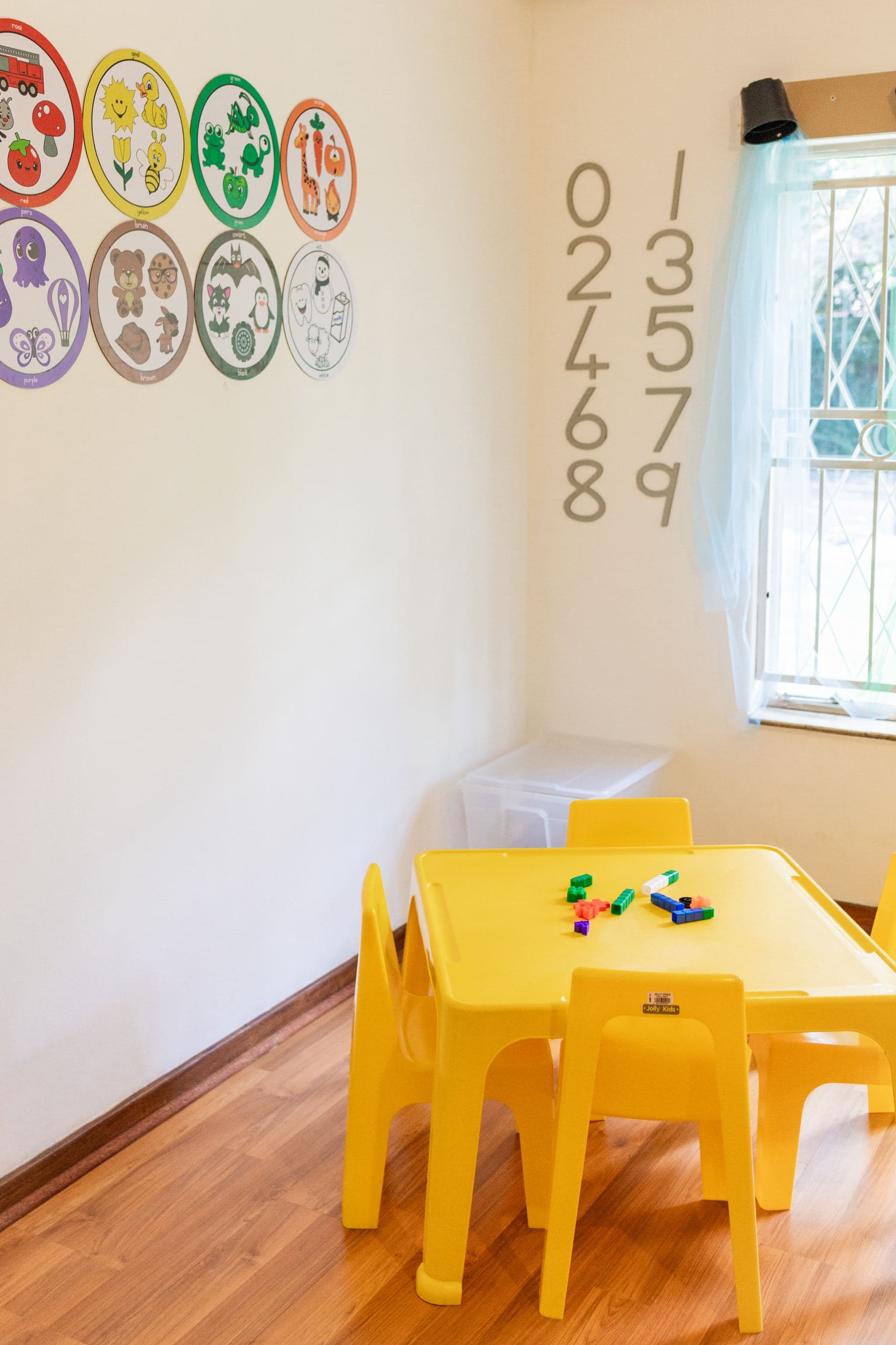 Classroom wall with bilingual colour-and-animal learning posters, above a table with building blocks