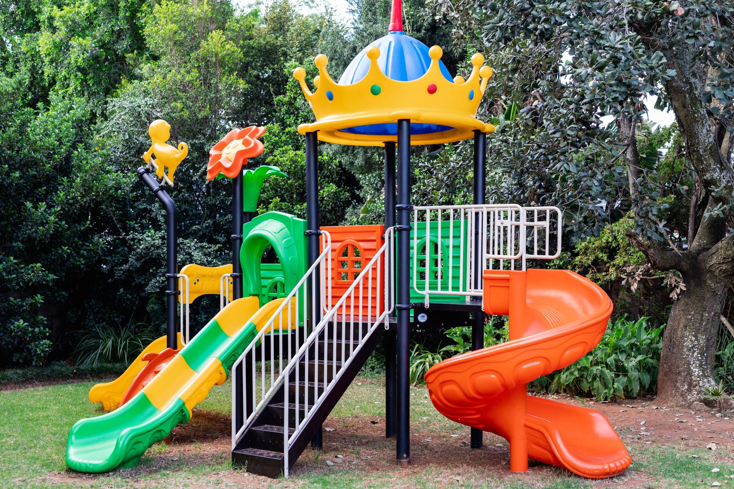 Outdoor jungle gym with a crown-shaped roof, spiral slide and climbing tower, surrounded by trees
