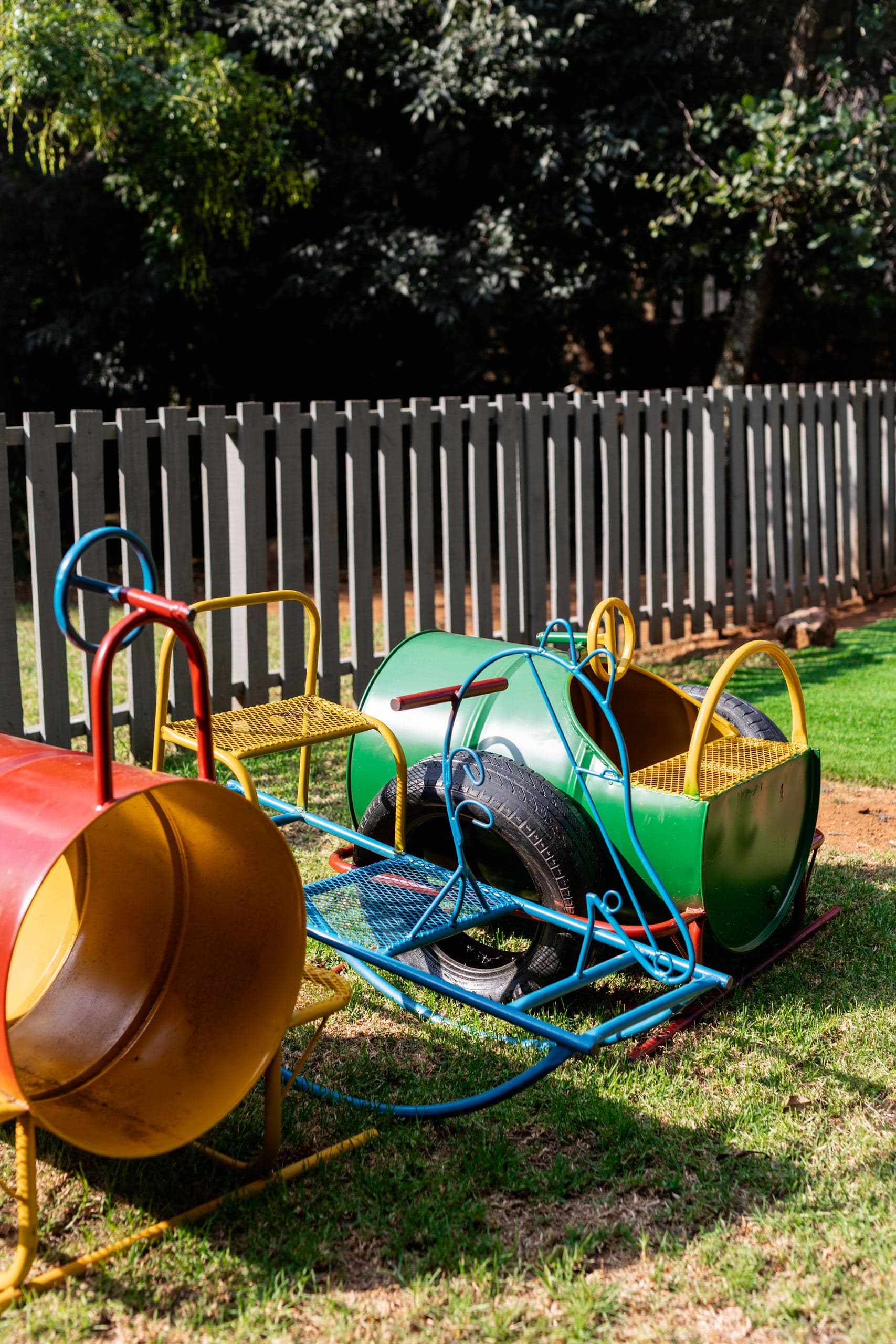 Colourful toddler ride-on play equipment on the grass, next to a wooden picket fence