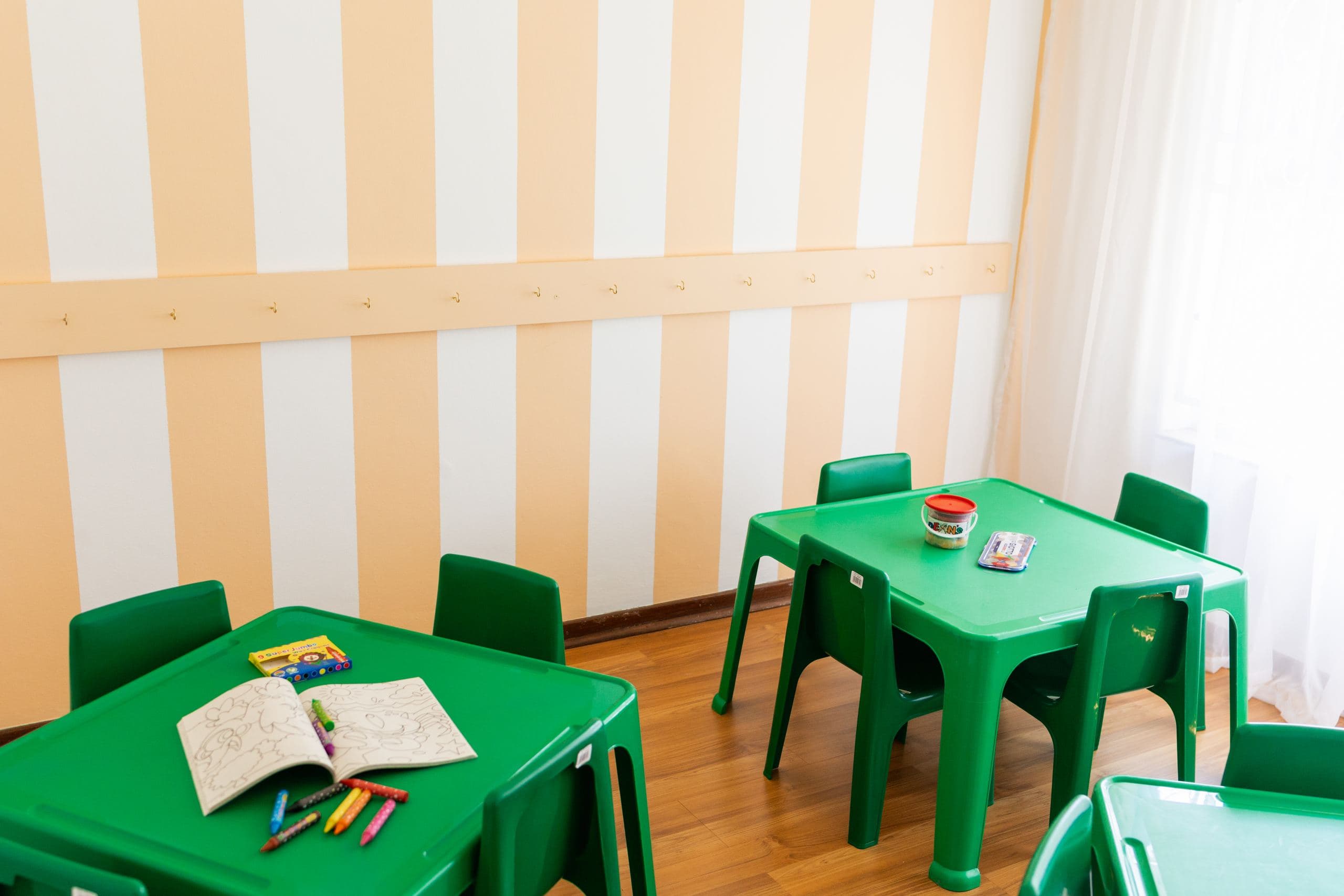 A playroom with green children's tables and chairs set up for colouring