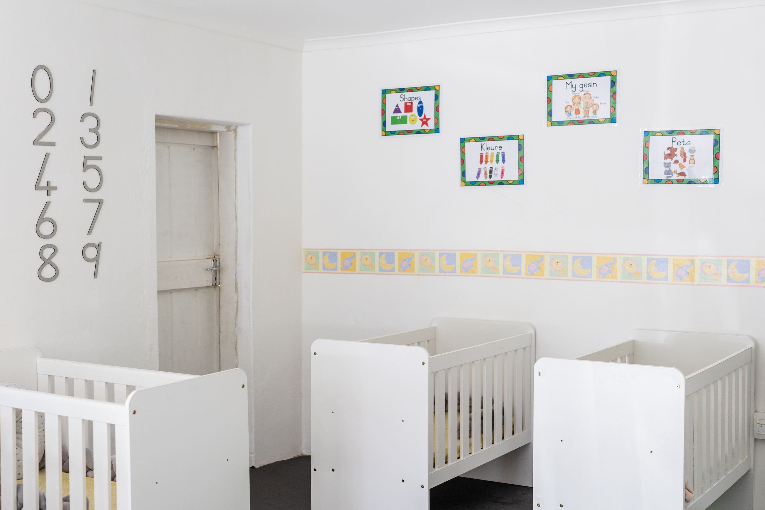 Classroom posters for shapes, colours, family and pets on the wall above cots in the baby room