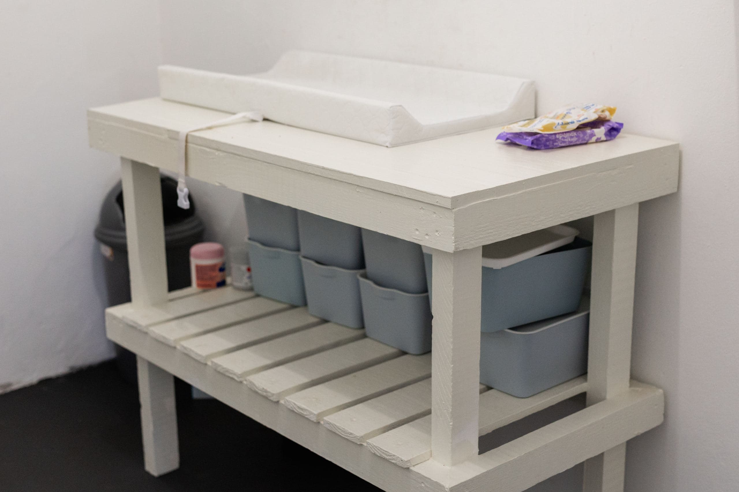 A baby's nappy-changing table with wipes and storage bins underneath