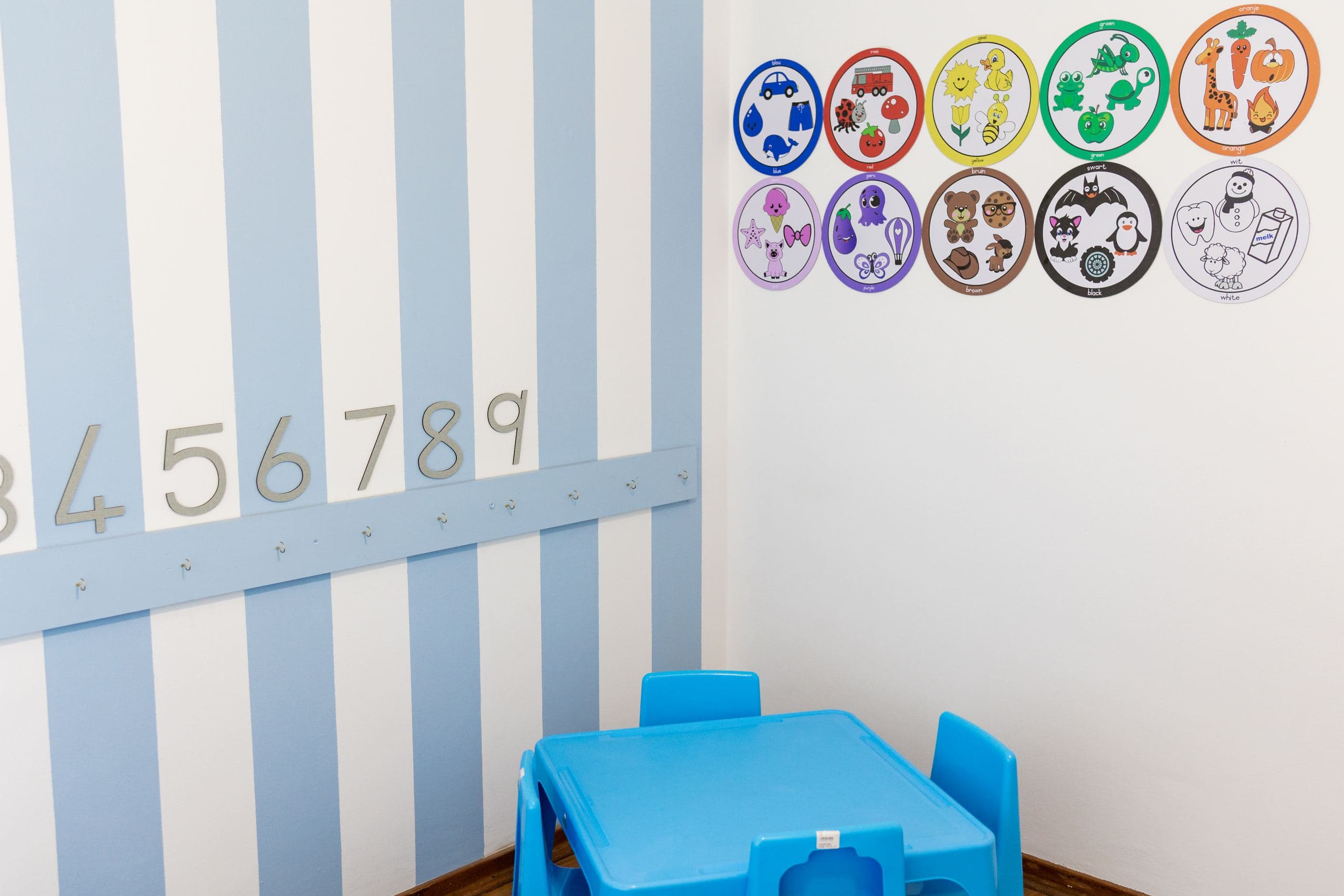 Classroom wall with bilingual colour-and-object learning posters, above a blue children's table