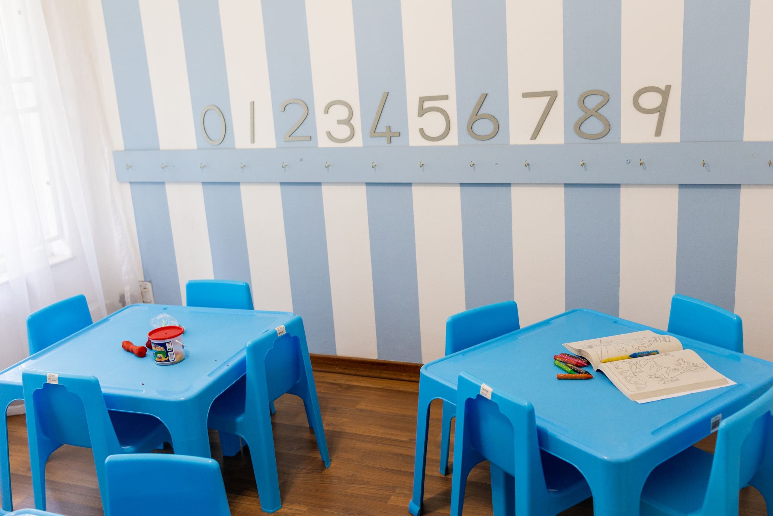 Wall-mounted number decorations above blue children's tables set up with colouring books